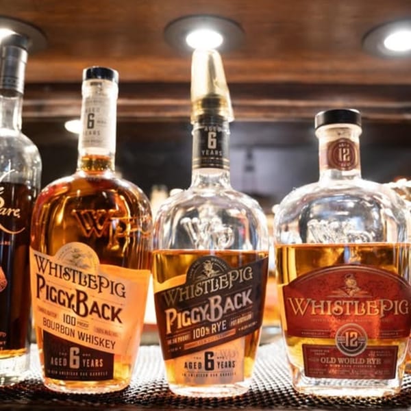 Three bottles of WhistlePig whiskey, including PiggyBack Bourbon and Old World Rye, on a bar.