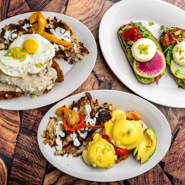 Three plates of breakfast food, including avocado toast, eggs benedict, and fried eggs with hash browns.
