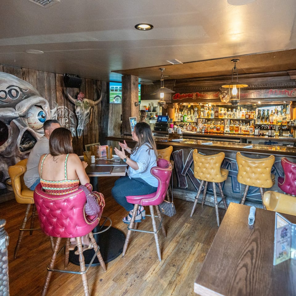 Patrons seated at a high-top table and bar in Krazy Kooters, with a large skull mural.