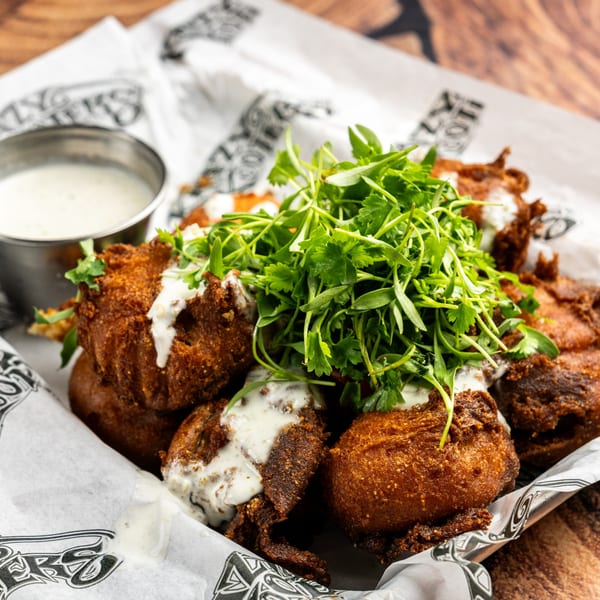 Krazy Kooters' fried hush puppies with creamy sauce and fresh greens, served in a basket.