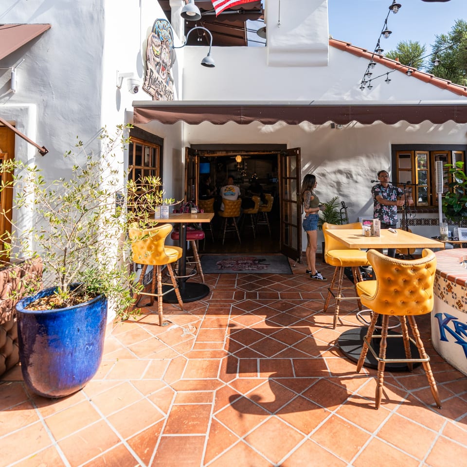 Krazy Kooters' outdoor patio with terracotta tiles, yellow bar stools, and people near the entrance.