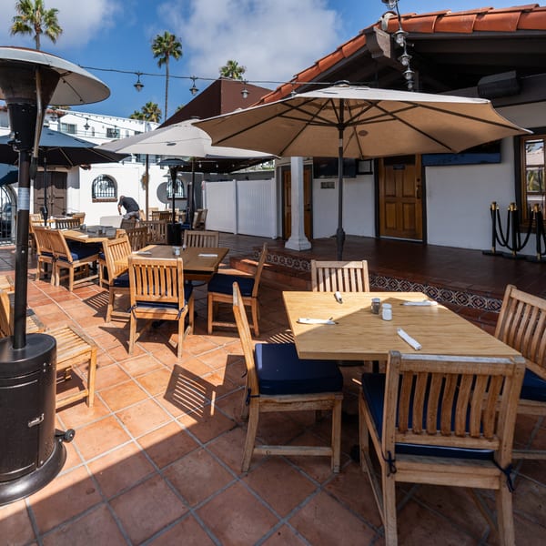 Krazy Kooters' outdoor patio with wooden tables, chairs, umbrellas, and a tiled floor under a blue sky.