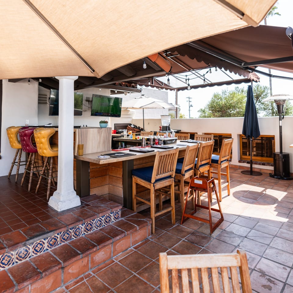 Krazy Kooters' outdoor patio features a bar, dining tables, and TVs under large umbrellas.
