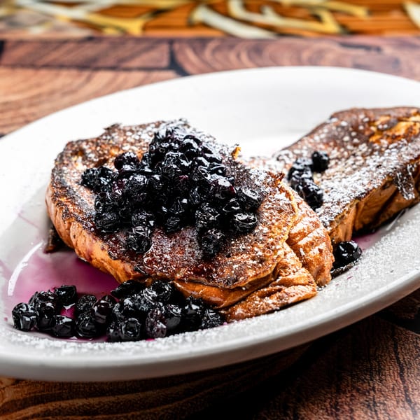 Golden French toast topped with dark blueberries and powdered sugar on a white plate.
