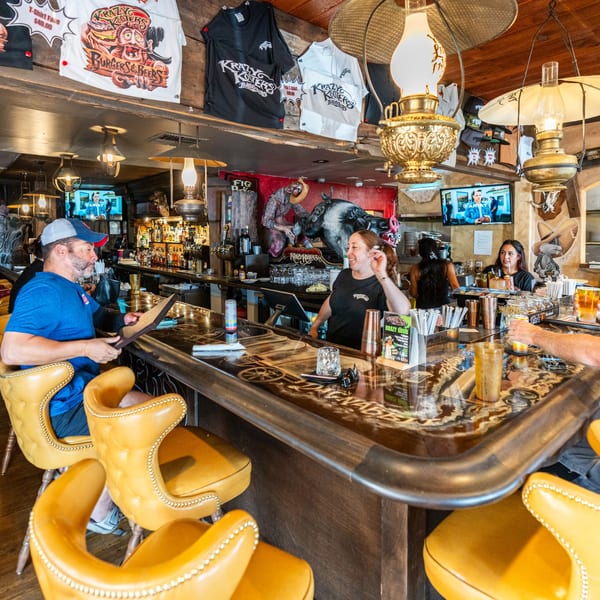 Krazy Kooters bar with patrons, a bartender, and Krazy Kooters merchandise hanging above.