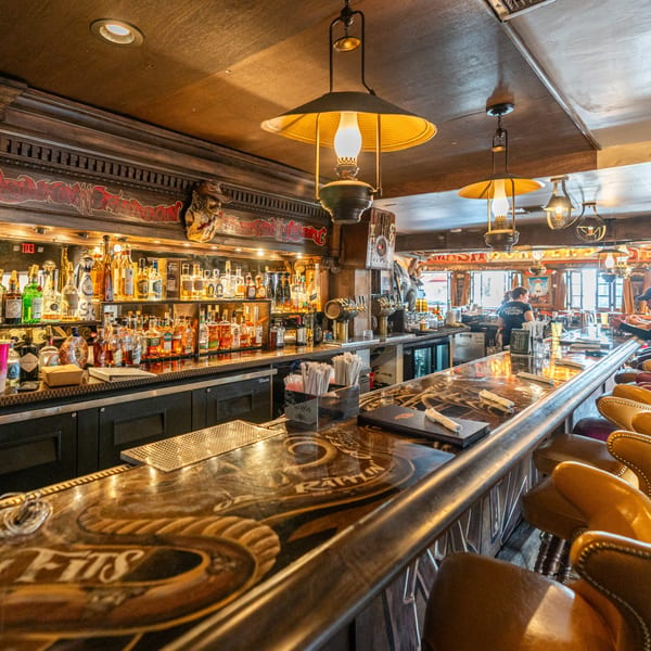 A long, dark wooden bar with bottles of liquor, beer taps, and leather stools at Krazy Kooters.