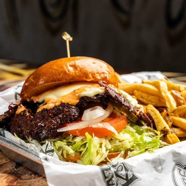 A Krazy Kooters burger with lettuce, tomato, onion, cheese, sauce, and bacon, served with fries.
