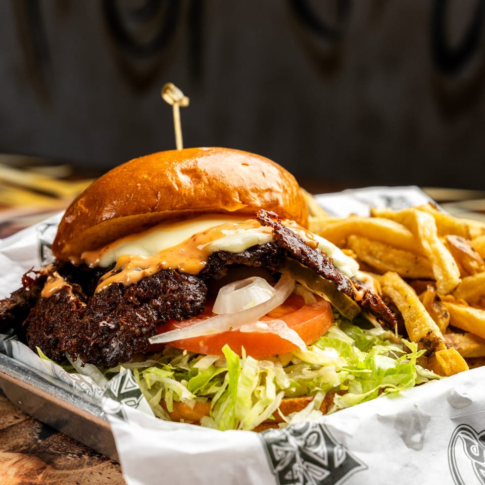 A Krazy Kooters burger with lettuce, tomato, onion, cheese, sauce, and bacon, served with fries.
