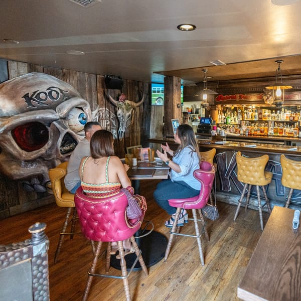 Three people seated at a high-top table in Krazy Kooters, with a bar and skull decor.