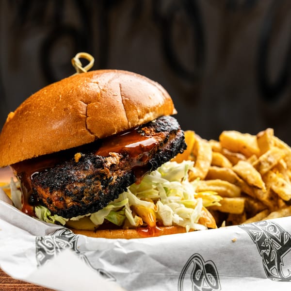 A Krazy Kooters burger with a dark patty, lettuce, and sauce, served with fries.