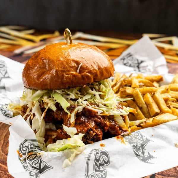 A Krazy Kooters burger with coleslaw and sauce, served with a side of golden fries.