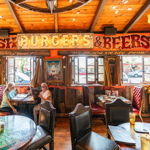 Two women reading menus inside Krazy Kooters, a rustic burger and beer restaurant with neon signs.